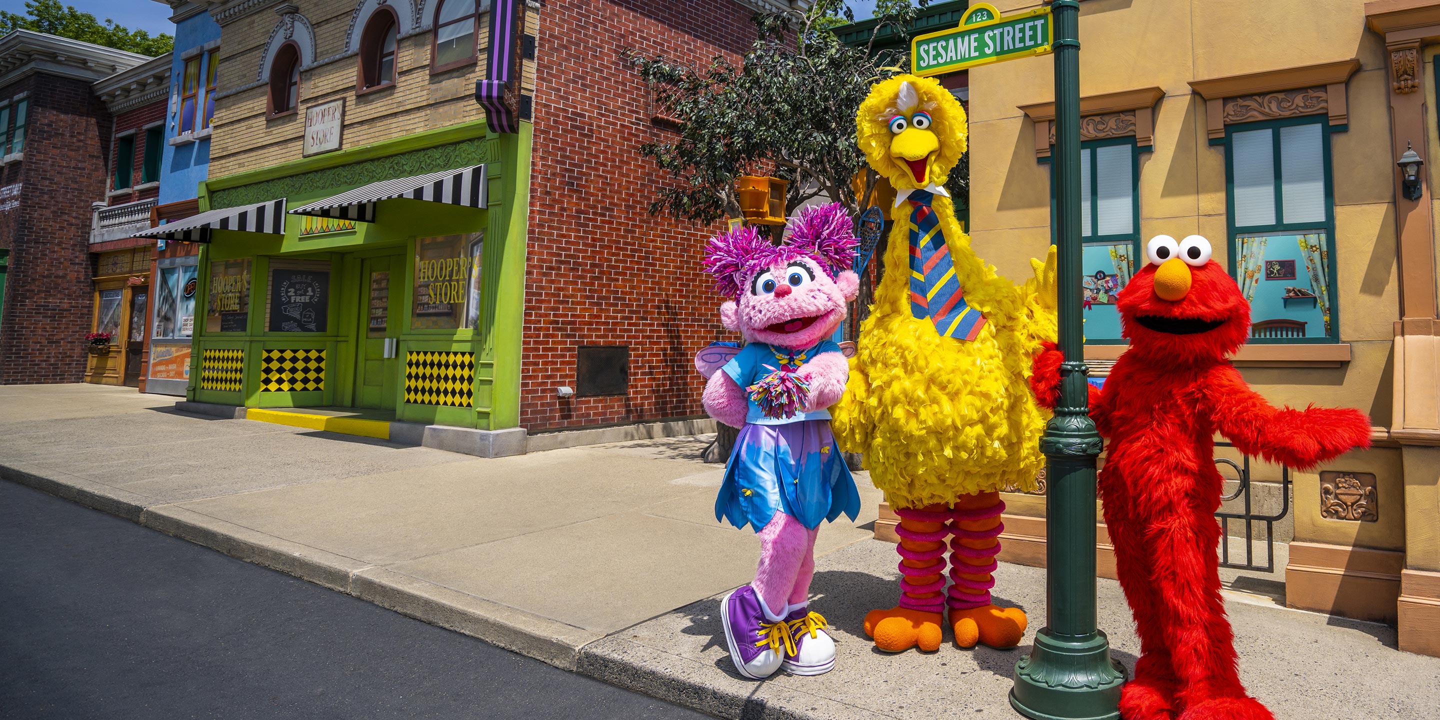Big bird, Elmo and Abby Cadabby on the street next to Sesame Street sign